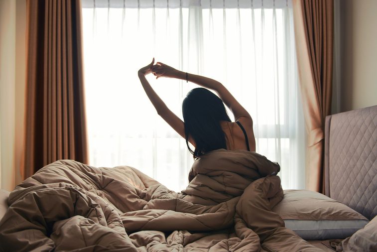Happy woman back view waking up stretching in bed room hotel