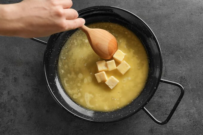 Woman stirring melting butter on frying pan, closeup