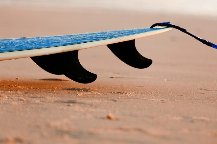 Tail of a surfboard on the sand with three fins