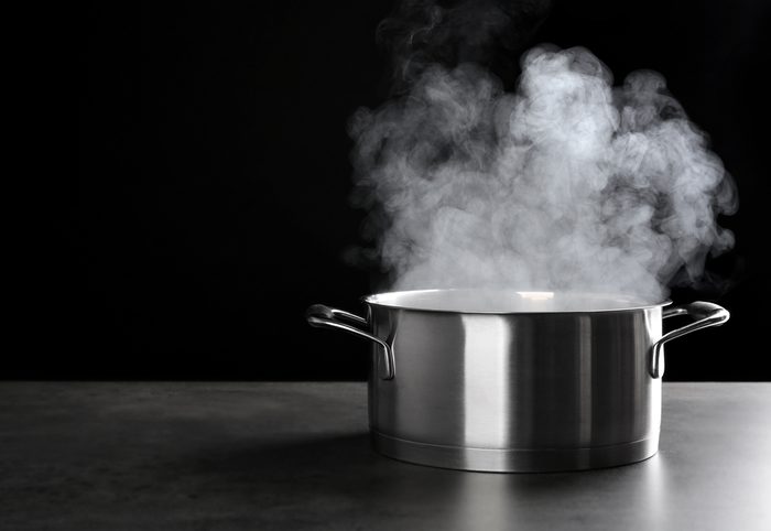 Metal saucepan with hot liquid on table against dark background