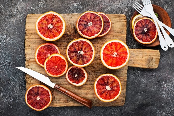 Fresh red oranges with slices on a vintage old cutting wooden board on a gray background. Top View