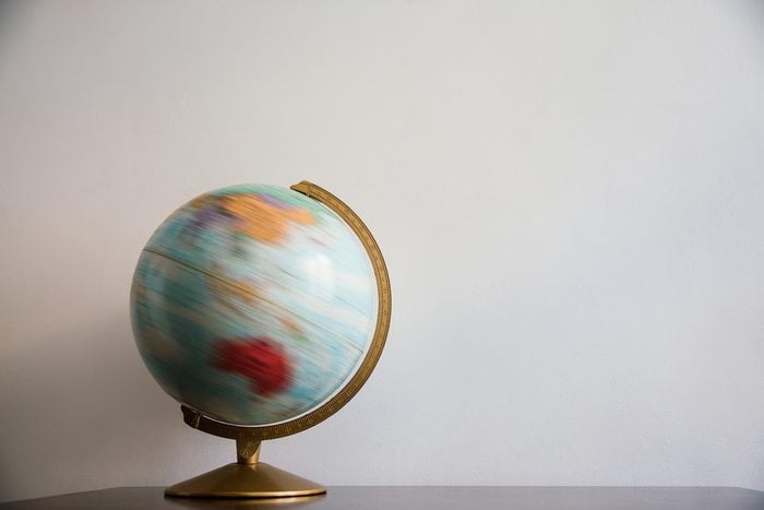 Globe model spinning on dark wooden desk. White wall empty space background.