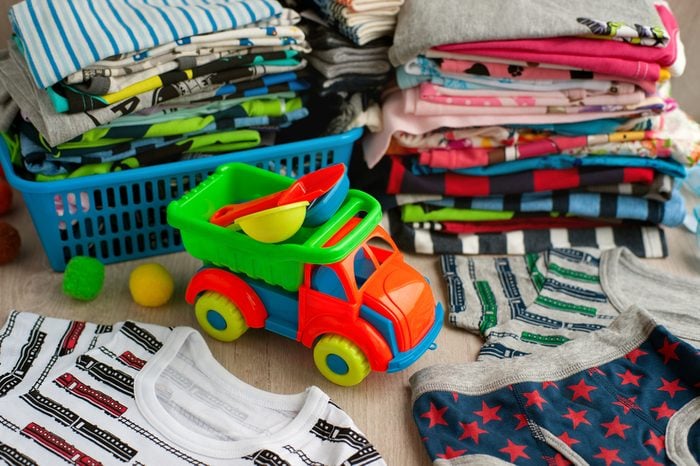 Many children's clothes. Clothes for children are stacked in the laundry basket and in a pile. Children's clothing made of soft fabric. Toy dump truck and clothes for the boy. T-shirts and panties.