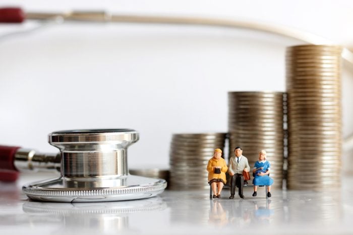 Miniature people sitting on syringe wit stethoscoper and stack of coins, business and health care concept.