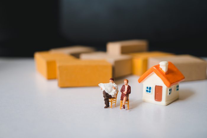 Miniature people, husband and wife relaxing on mini house and stack cardboard boxes background using as logistics and home business concept