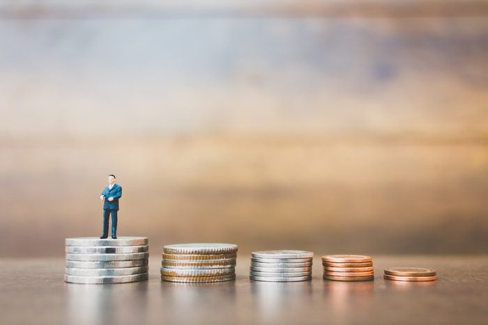 Miniature people businessman standing on money with wooden background