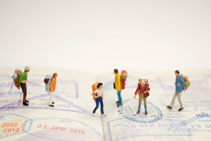 Miniature figure : Close up of group of younger traveler standing on visa stamps , backpack and travel concept. 