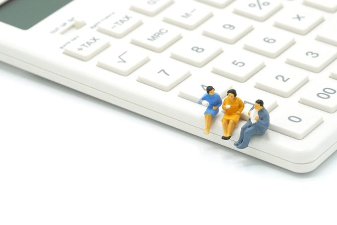 Miniature 3 people sitting on white calculator using as background business concept with copy space.