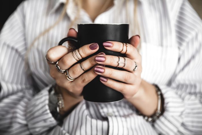 Female hands holding a white cup of tea, burgundy manicure, the girl is dressed in a shirt