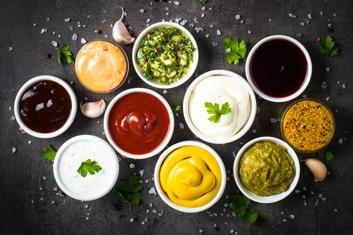 Set of sauces - ketchup, mayonnaise, mustard soy sauce, bbq sauce, pesto, chimichurri, mustard grains and pomegranate sauce on dark stone background. Top view.