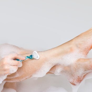 Woman shaving legs with razor in bathroom at home