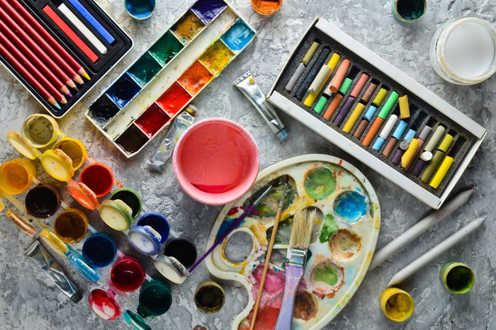 Artistic tools for drawing paintings on a gray concrete background. Palette, gouache, oil paint, brushes, colored crayons, pastel, colored pencils. Top view.