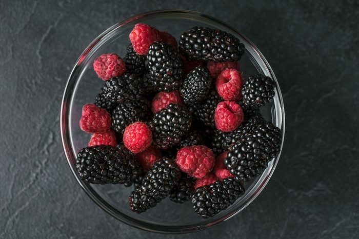 Glass plate with ripe red blackberries and raspberries on a black surface. Macro photo of ripe blackberries and raspberries.