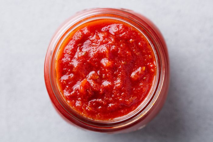 Tomato sauce in a glass jar. Top view. Grey background.
