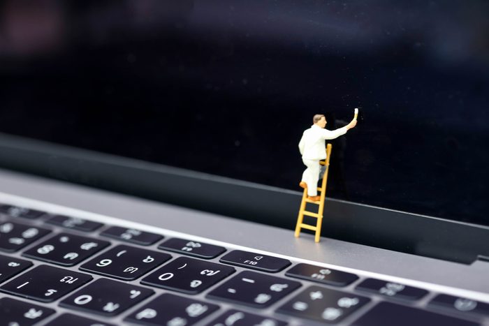 Miniature people : worker with ladder and painting in front of screen laptop.