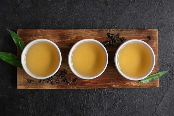 Green tea in ceramic cups, dry green oolong tea and tea leaves on black stone table, copy space.