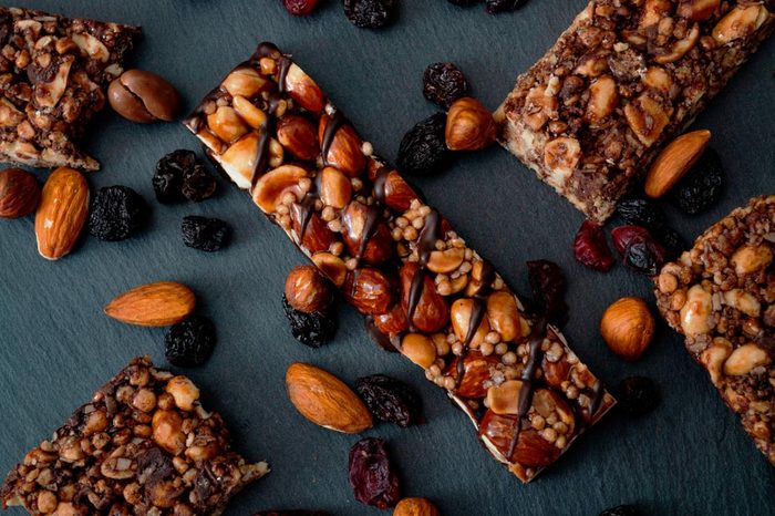 Healthy snacks, fitness lifestyle and high fiber diet concept with granola energy bars surrounded by dried fruits, hazelnuts and almonds on a black stone with dramatic light