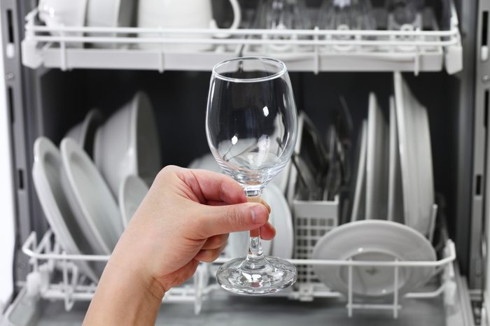 dishwasher, open and loaded with dishes, man hand taking out clean wine glass, after washing