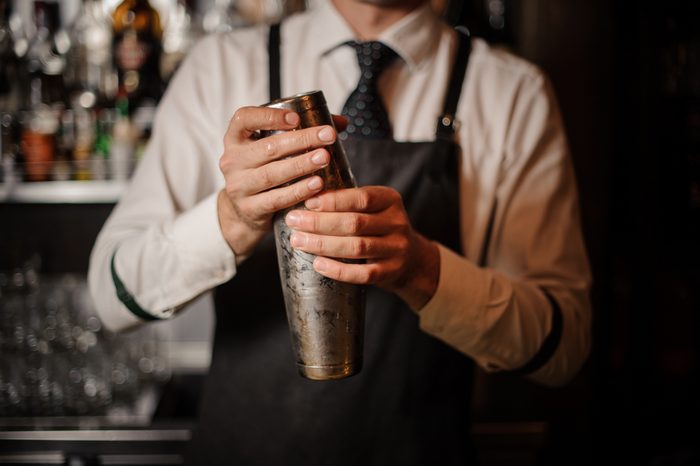 Professional male bartender holding a steel shaker ready to prepare a fresh cocktail at the bar counter