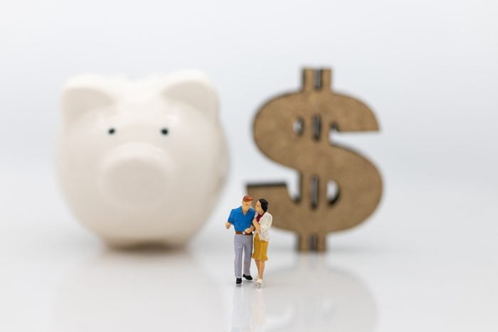 Miniature people : Couple standing area front of piggy bank and wooden dollar. Image use for Valentine's day , planning life after marriage concept.