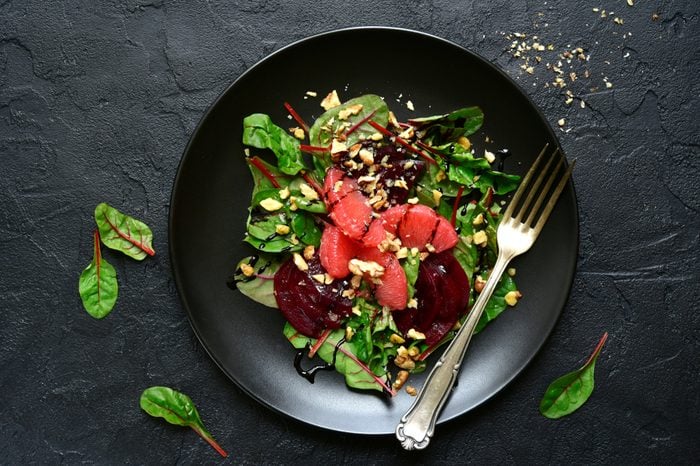Delicious salad with chard leaves, beetroot and grapefruit slices on a black plate over dark slate, concrete or stone background.Top view.