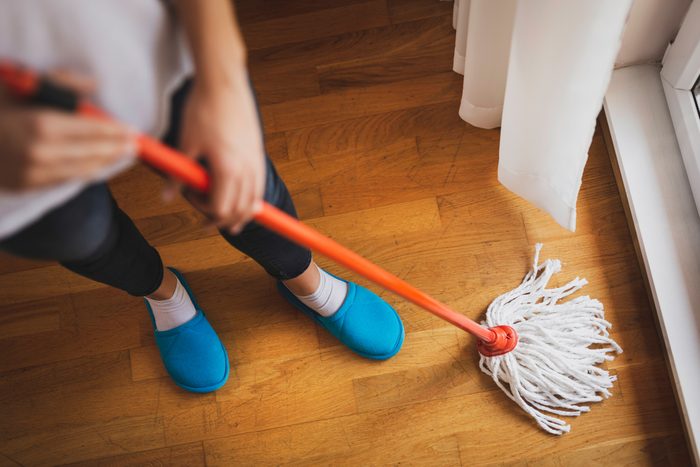 High angle view of woman holding a floor wiper and wiping floor, keeping the daily home hygiene. Focus on the mop