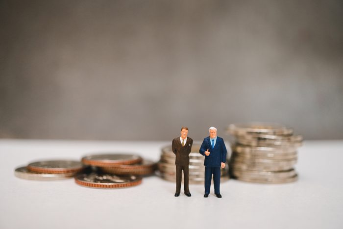 Miniature people, couple businessman standing on pile coins background using as business corporation and financial concept