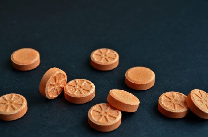 Orange round orange shaped tablets are scattered chaotically on black background with copyspace