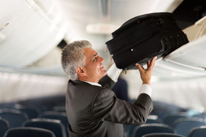mature businessman putting luggage into overhead locker on airplane