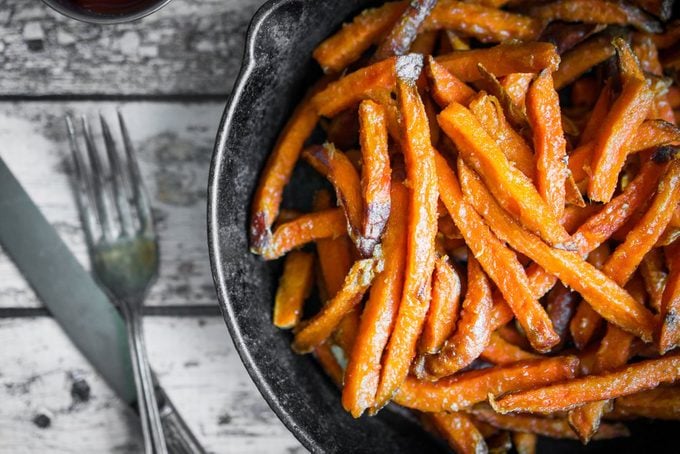 Sweet potato fries in cast iron skillet on wooden background