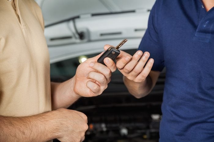 Midsection of male client giving car key to mechanic in auto repair shop