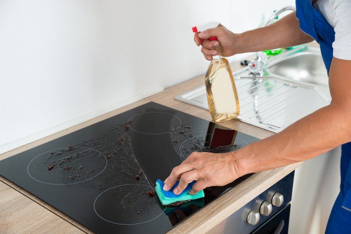 Cropped image of male janitor cleaning induction stove in kitchen