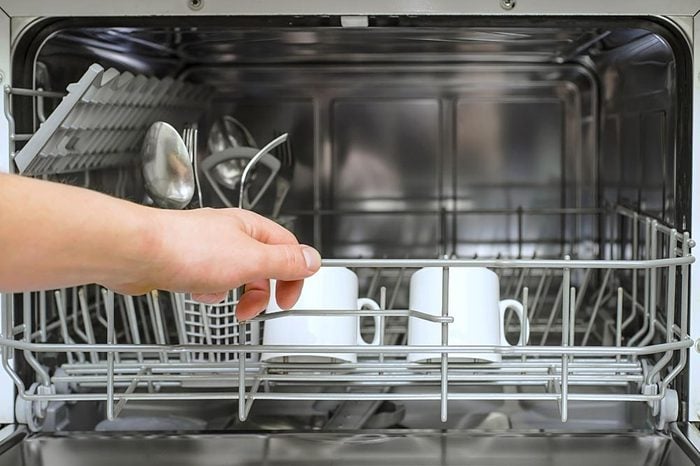 Open dishwasher with clean utensils in it, man hands loading dishes to the dishwasher machine, introducing or taking out a plate and cup, clean tableware after cleaning process