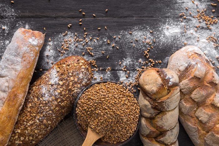 Bread border on dark wood with copy space background. Brown and white whole grain loaves still life composition with wheat flour sprinkled around. Bakery, cooking and grocery store concept.