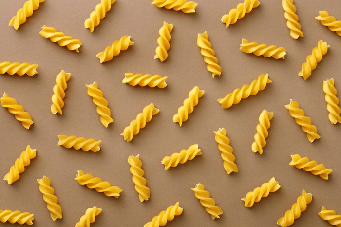 Top view of spiralli pasta pattern.Flat lay raw spilled Italian pasta view from above on neutral background. Repetition concept.