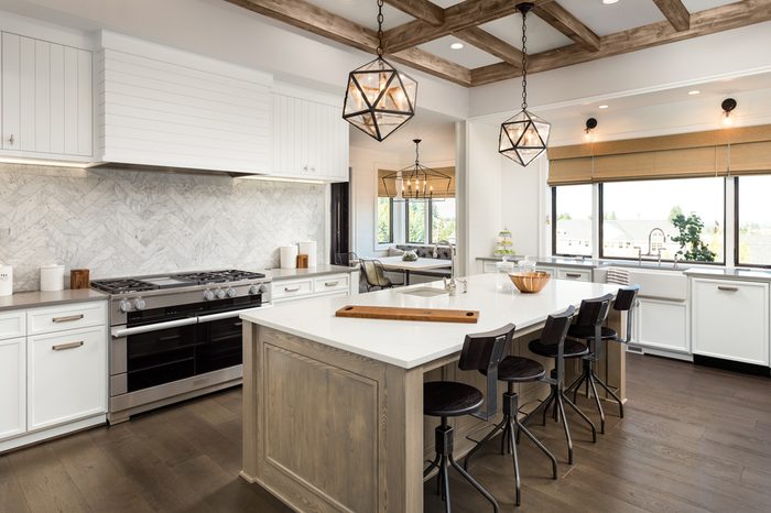 Kitchen Interior with Island, Sink, Cabinets, and Hardwood Floors in New Luxury Home. Features Elegant Pendant Light Fixtures, and Farmhouse Sink next to Window