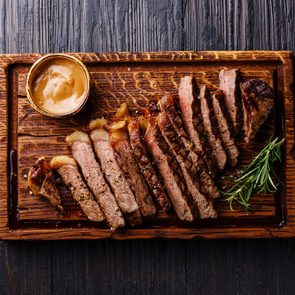 Sliced grilled well done Striploin steak with Pepper sauce on cutting board on burned black wooden background
