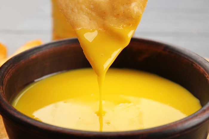 Dipping chips into bowl with creamy cheese sauce, close up