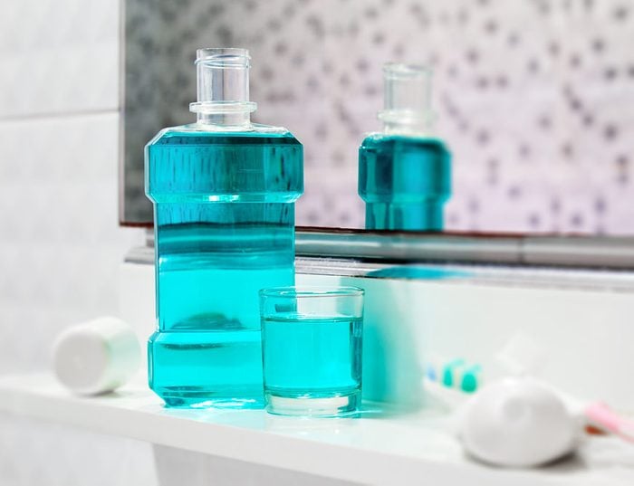 Oral cleanser for good oral health, Bottle and glass of mouthwash on bath shelf with blurred toothbrush and toothpaste in foreground