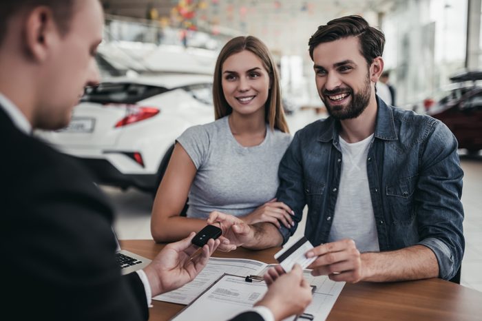 Happy beautiful couple is buying a new car at dealership. Credit card in hand.
