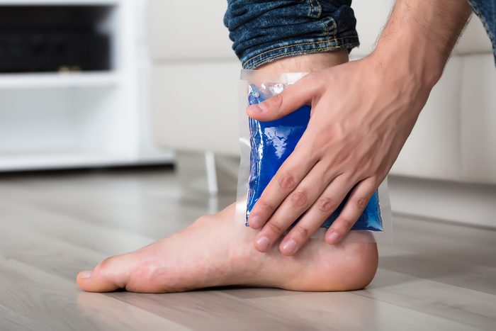 Close-up Of Person's Hand Holding Ice Gel Pack On Ankle At Home