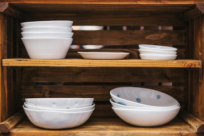 Many ordinary ceramic plates on wooden shelves. Kitchen accessories for cooking.