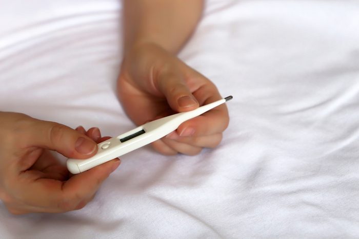 Digital thermometer in female hands close up on the bed. Measuring body temperature, concept of cold and flu, fever, illness