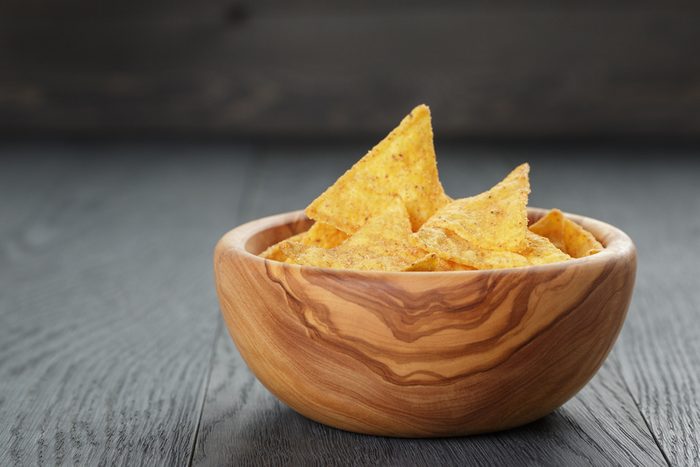 tortilla chips in olive wood bowl on wooden table, selective focus