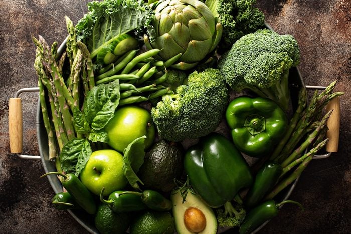 Variety of green vegetables and fruits on a tray, dark setting overhead shot
