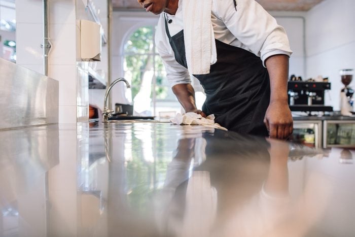 Cropped shot of waiter wiping the counter top in the kitchen with cloth. Man cleaning and maintaining commercial kitchen hygiene.