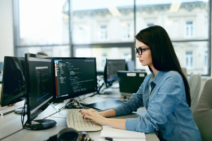 Young Woman Working And Programming On Computer In Office. Beautiful Female Programmer Working Looking At Monitor, Typing Data Code In Company Office. High Quality Image.