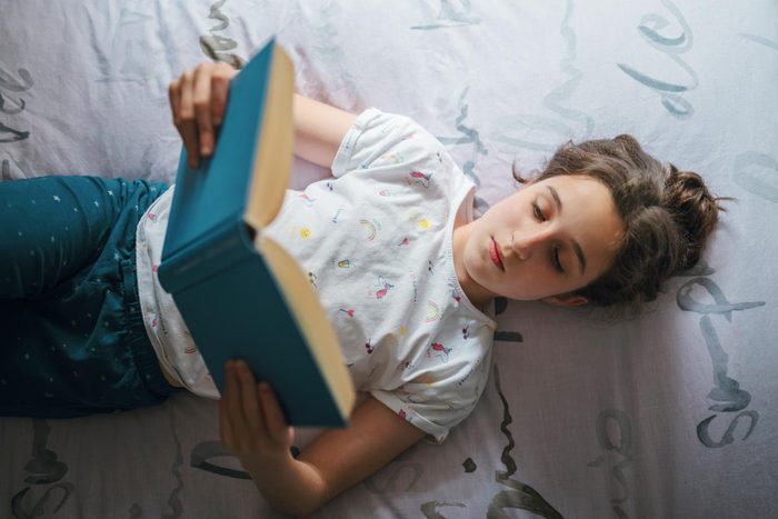 young girl reading a book on her bed