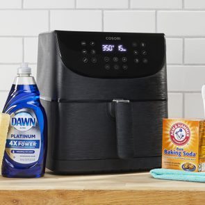 air fryer, center, on a kitchen counter surrounded by the supplies needed to clean the appliance