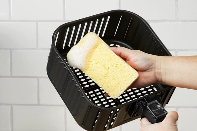 close up cleaning the basket of an air fryer with a sponge